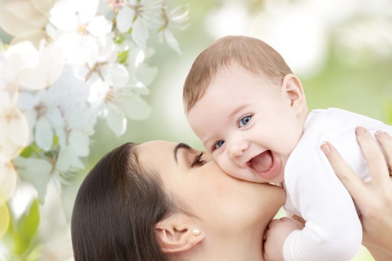 family, motherhood, children, parenthood and people concept - happy mother kissing her baby over cherry blossom background